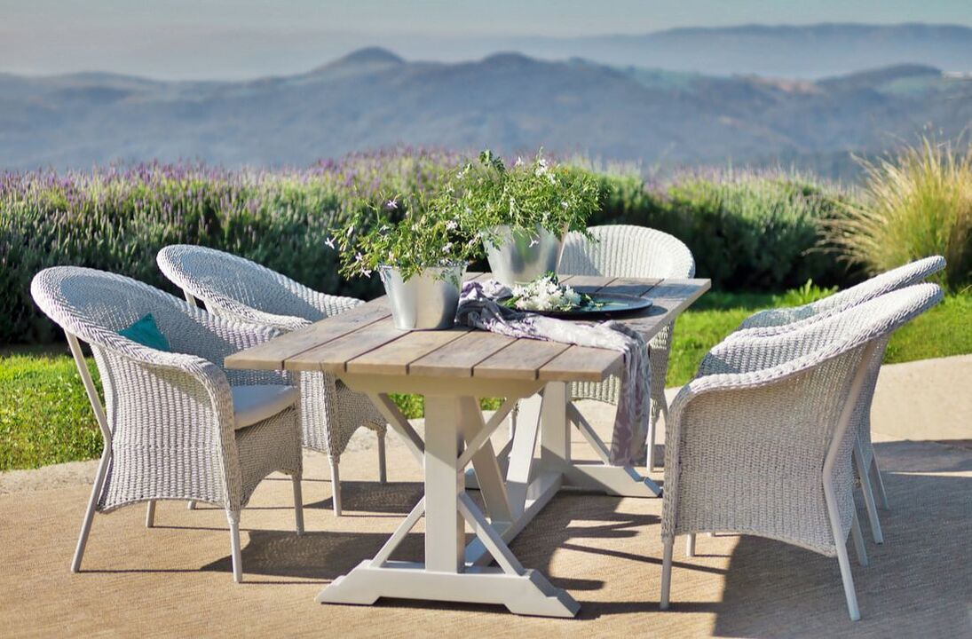 garden set of big teak table with six weaved armchairs Classic style and ash colour with flowers in a metal buckets decoration with a mountains landscape background in Casares, Malaga, Andalucia, Spain