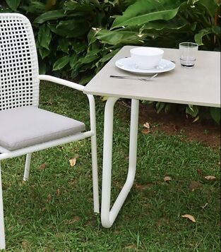 White rope weaved dining armchair with cushion and concrete top table in a garden lawn with big plants background in Estepona, Malaga, Spain
