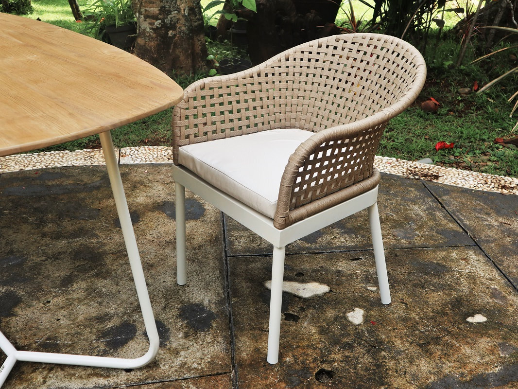 Aina outdoor dining armchair with natural nut fibre and aluminium next to an aluminium table with teak table top.
