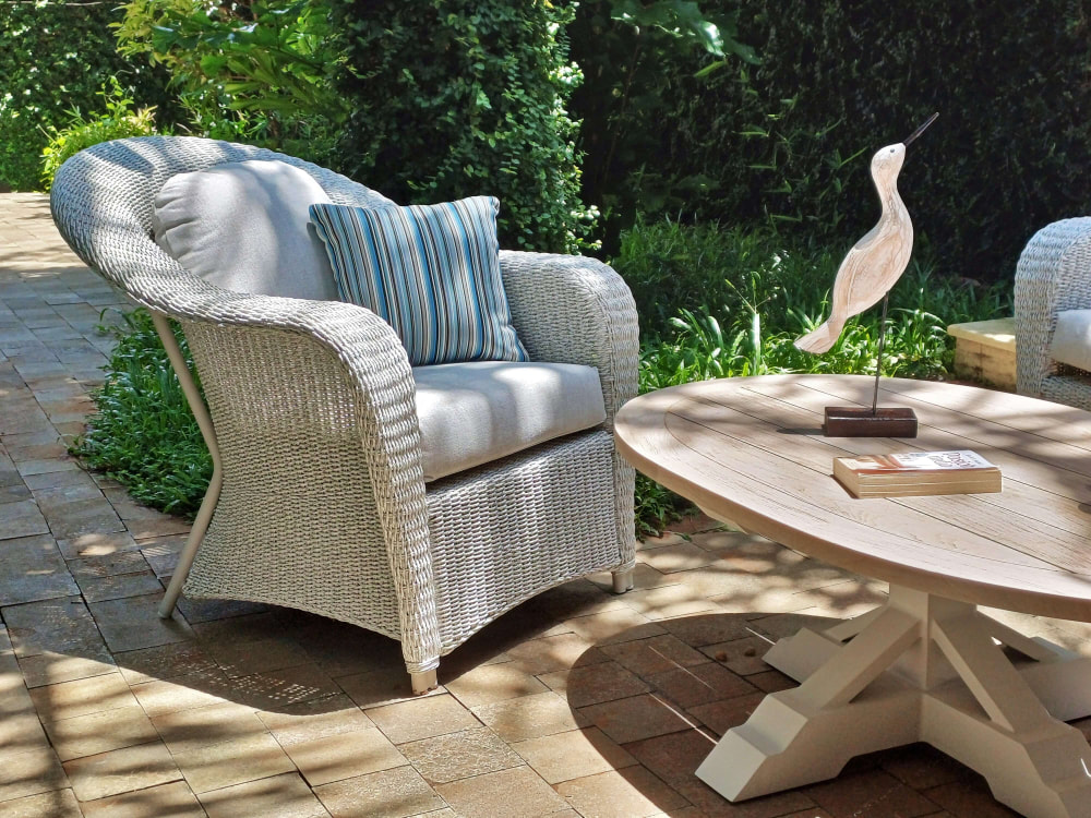 Fibre weaved armchair classin style in ash colour with stripped decorative cushion with teak coffee table with a wooden bird sculpture in a mature garden in Estepona, Malaga, Spain