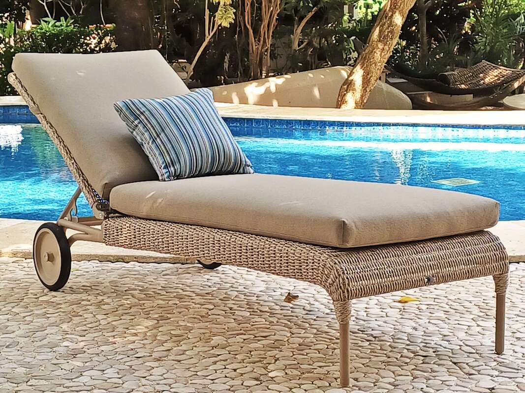 Weaved sunbed with wheels and cushion with a small decorative cushion in a pool area with white peebles floors in a tropical garden in Estepona, Malaga, Spain