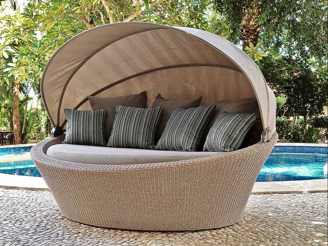 WEAVED DAYBED WITH CANOPY IN NATURAL COLOUR AND DECORATIVE STRIPED CUSHIONS IN A POOL TERRACE WITH WHITE STONES FLLOR AND BIG TREES GARDEN IN SOTOGRANDE